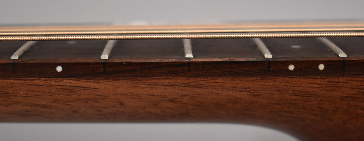 Close-up of the dark mahogany neck and fretboard, showing five frets, three side dots, and two bronze strings.
