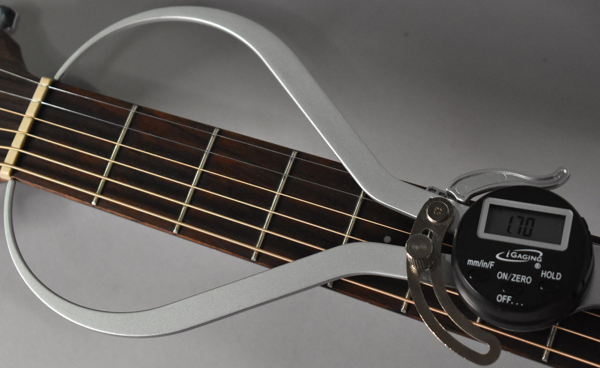 Close-up of the guitar's dark fretboard and light strings, with a silver digital caliper measuring the nut width at 1.70.