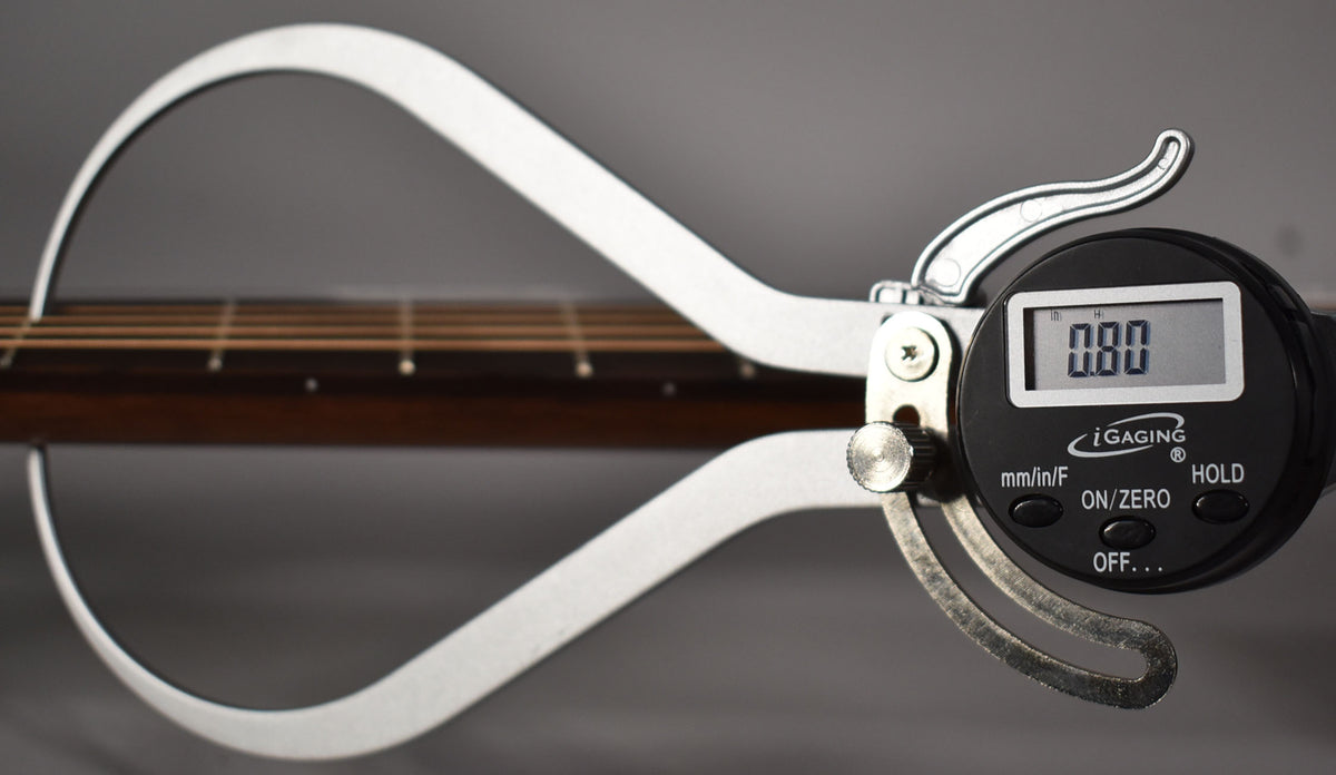 A digital caliper measures the guitar's dark brown fretboard and light strings, displaying "0.80" on its black screen.