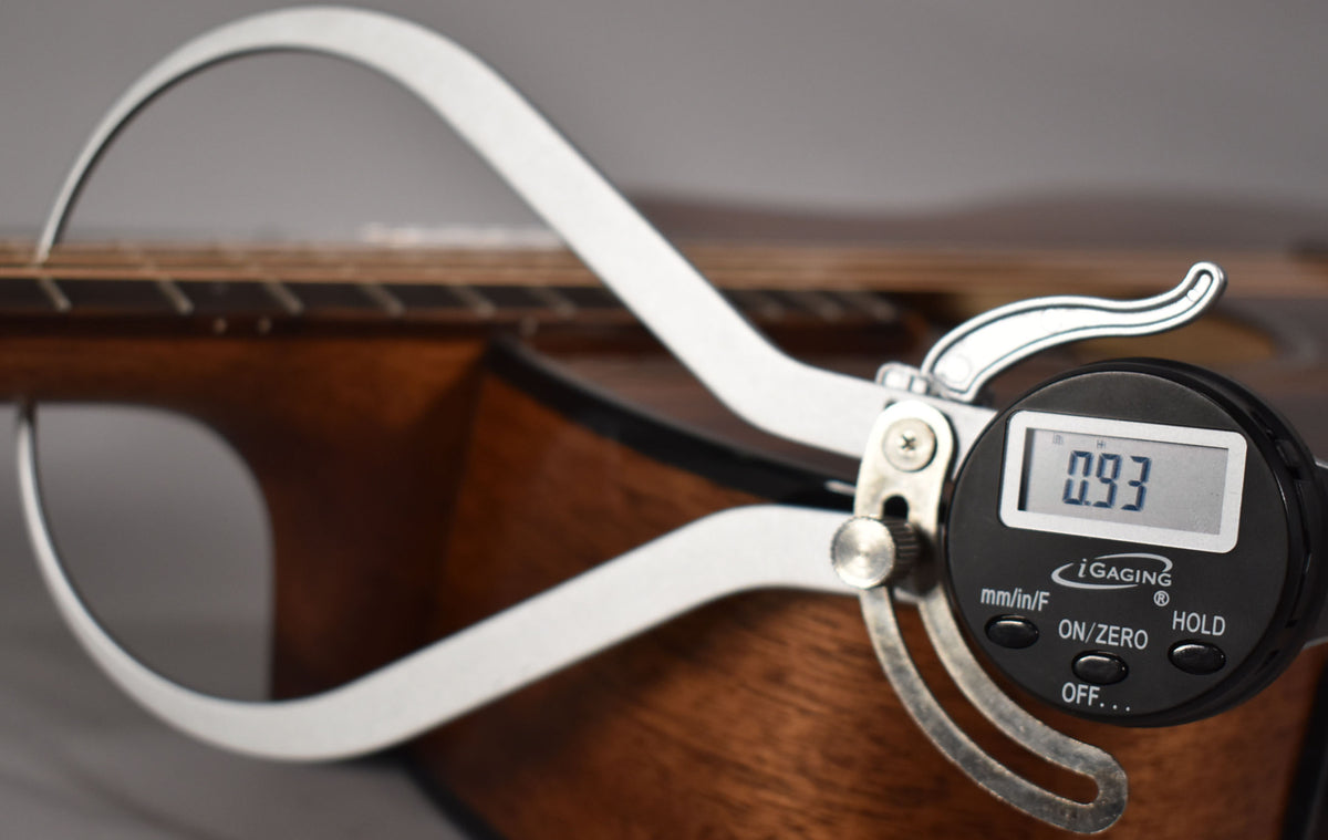 A digital caliper measures the guitar's fretboard, showing "0.93" on its screen, with the mahogany body visible below.