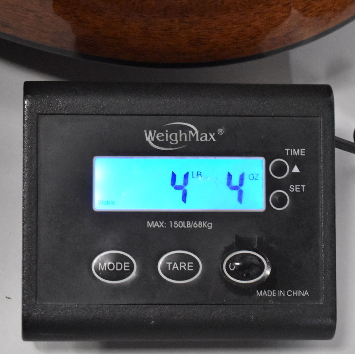 A black WeighMax scale displays "4 LB 4 OZ" on a bright blue screen, with the guitar's mahogany body visible at the top.