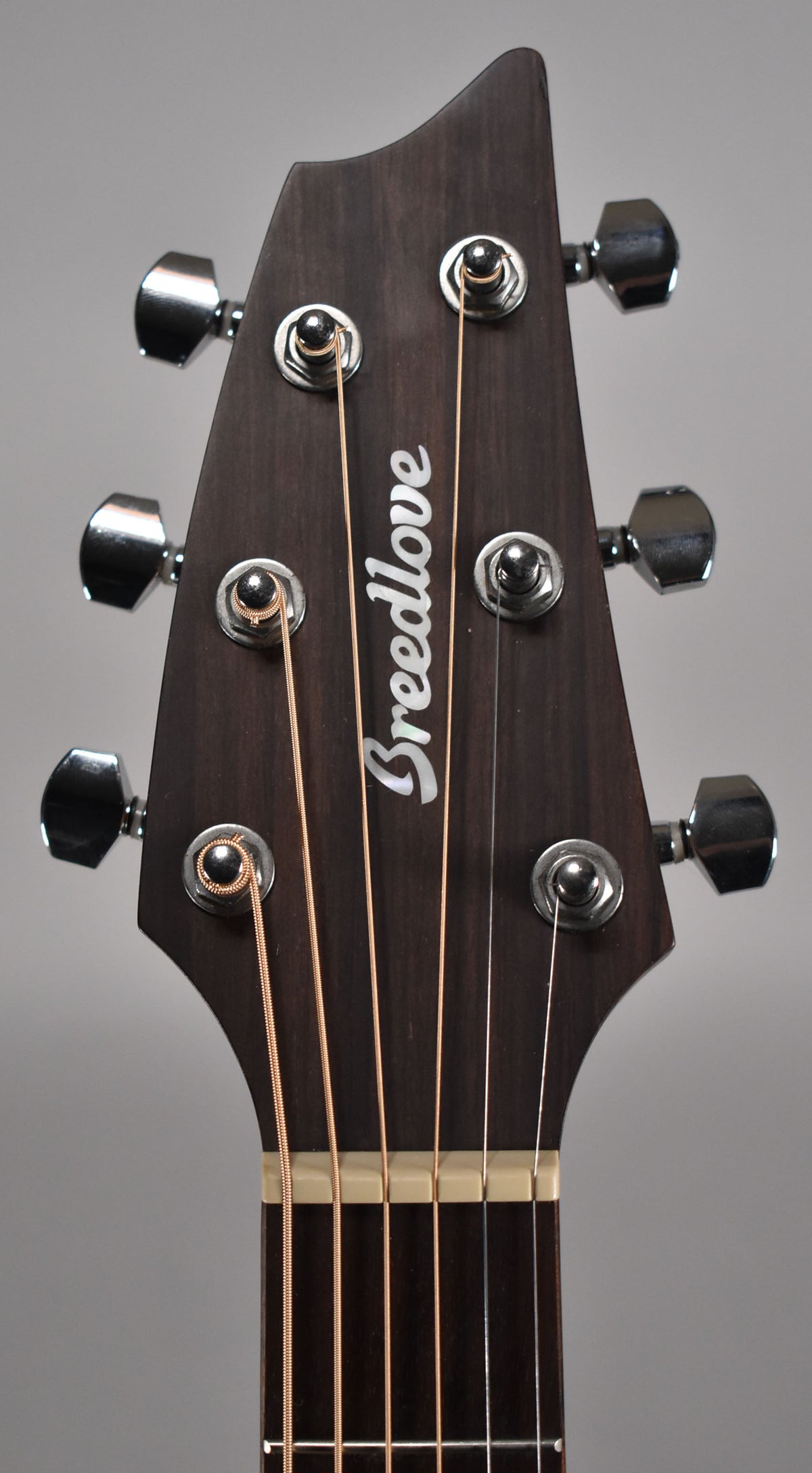 Close-up of the dark brown headstock with a satin finish, showing six chrome tuners and light-colored strings.
