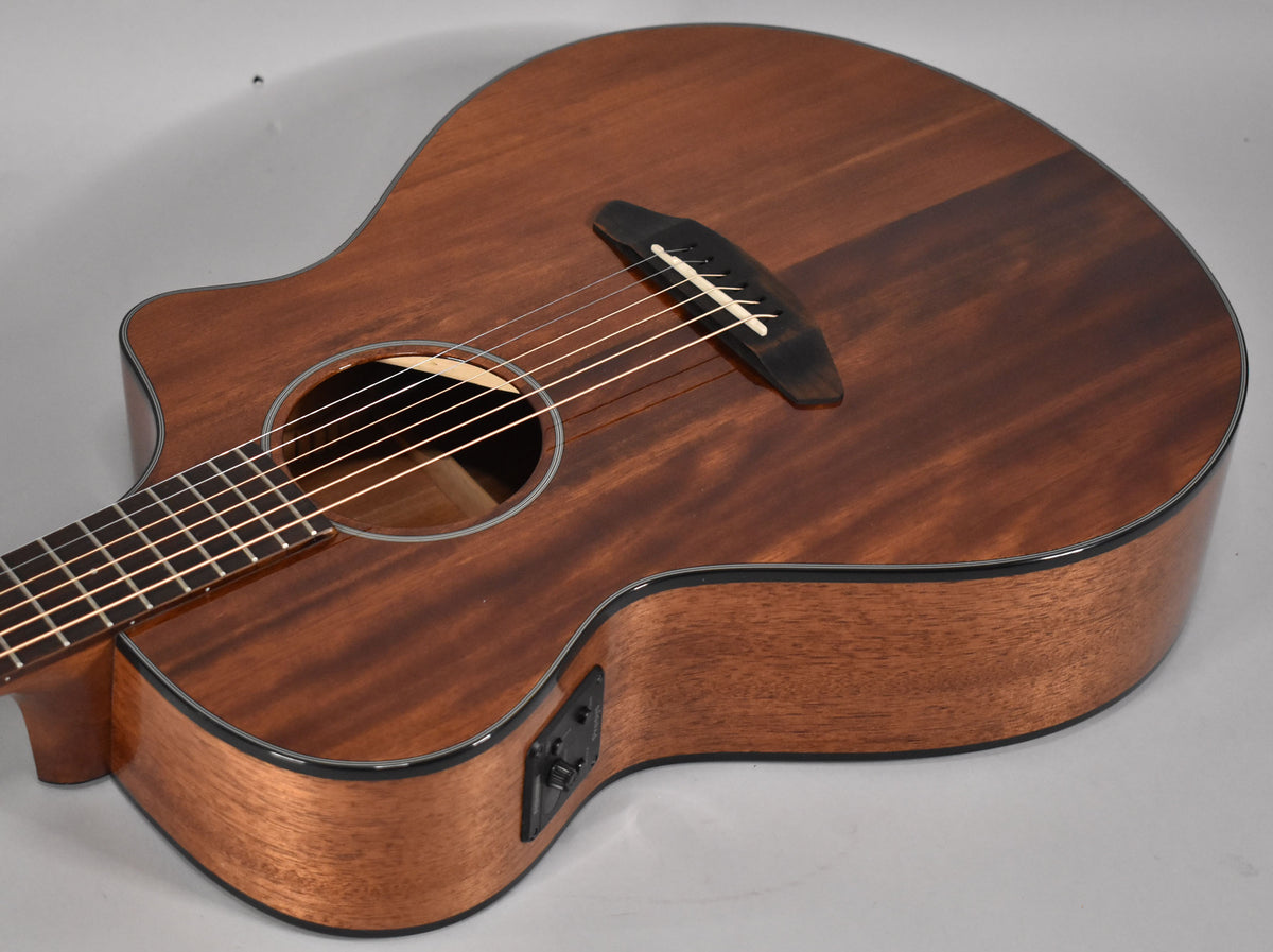 Acoustic guitar, angled from the upper bout, showing the dark brown body with a cutaway and black electronics on the side.