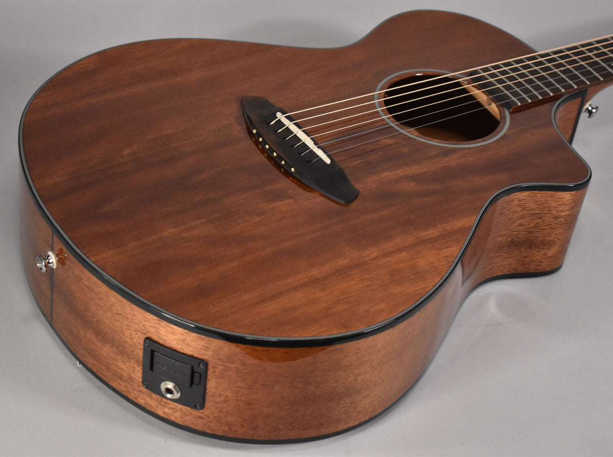 The mahogany acoustic guitar's body is angled from the lower left, showing the dark wood grain, black bridge, and output jack.