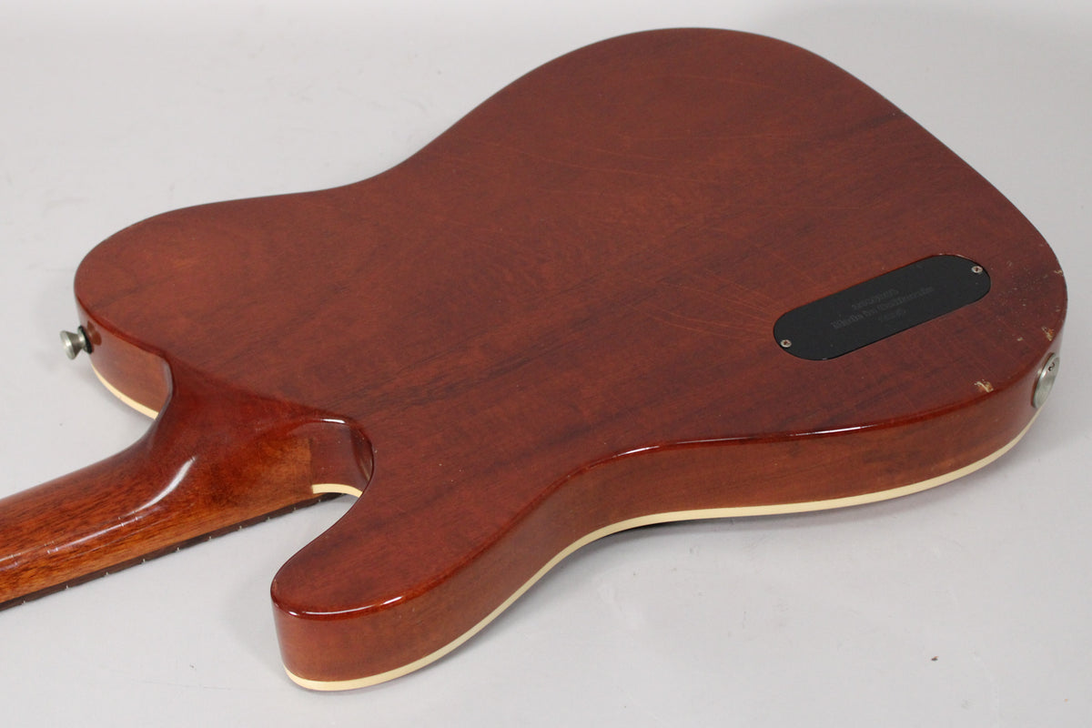 The guitar's amber nitro finish back shows a control cavity cover, cream binding, and some wear near the strap button.
