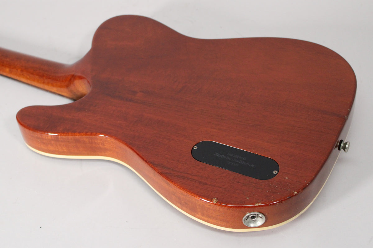 The guitar's amber nitro finish body and neck are viewed from the back, showing a black control plate and output jack.