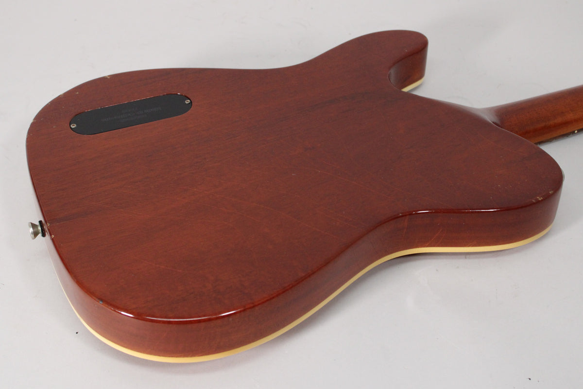 The guitar's amber nitro finish back shows light wear, with a black control cavity cover and a chrome strap button visible.