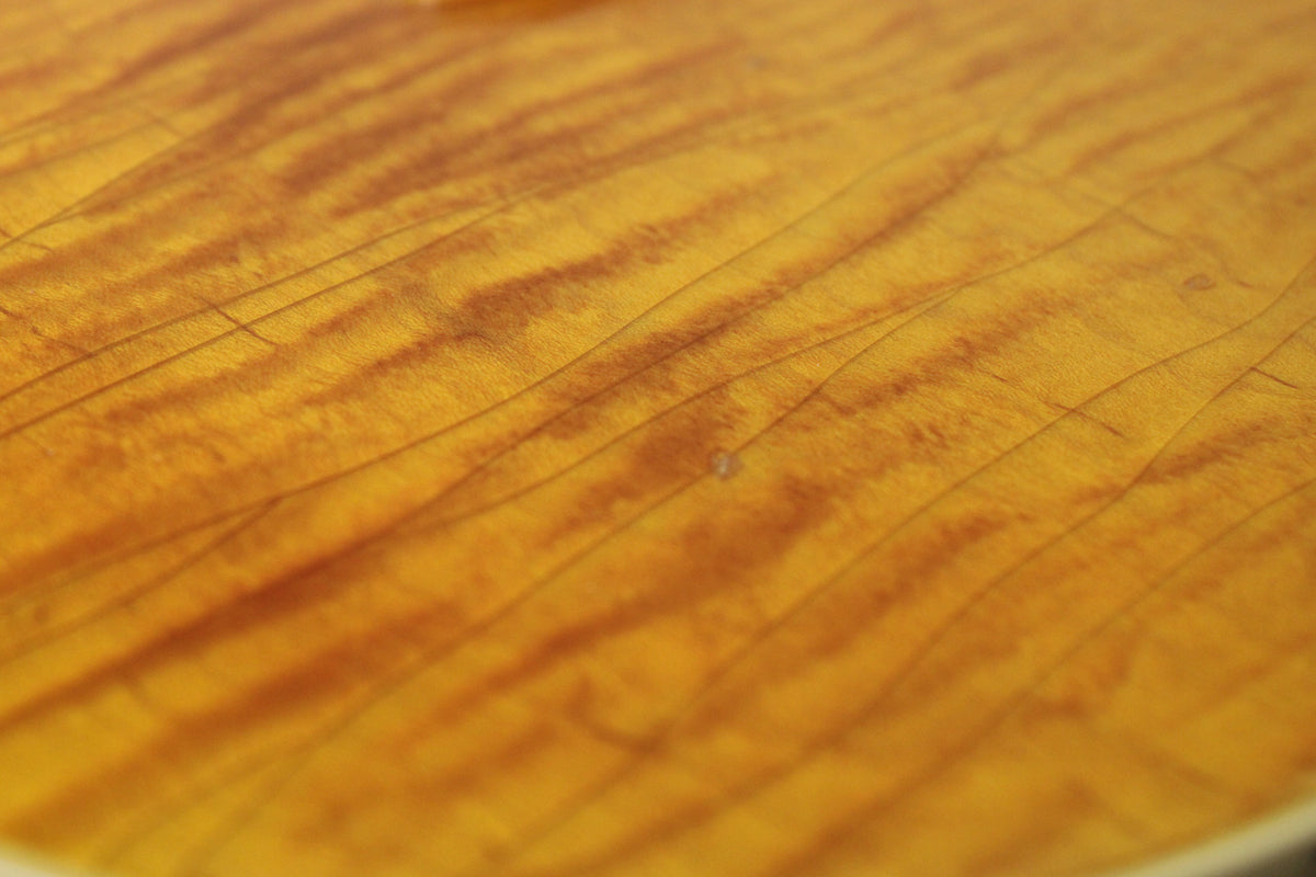 Close-up of the amber nitro finish, showing fine lacquer checking lines and a small ding on the highly figured maple top.