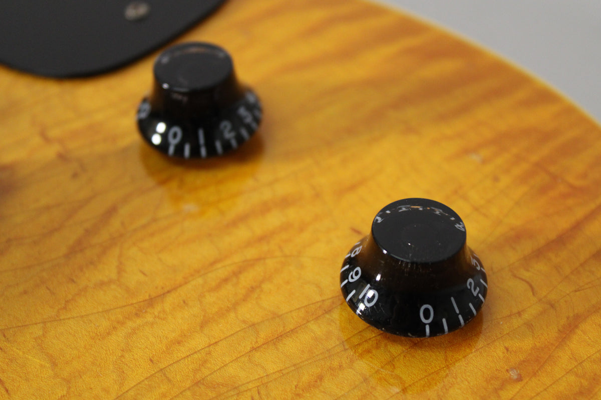 Close-up of two black bell-shaped control knobs with white numbers on the aged amber nitro finish, showing fine checking.