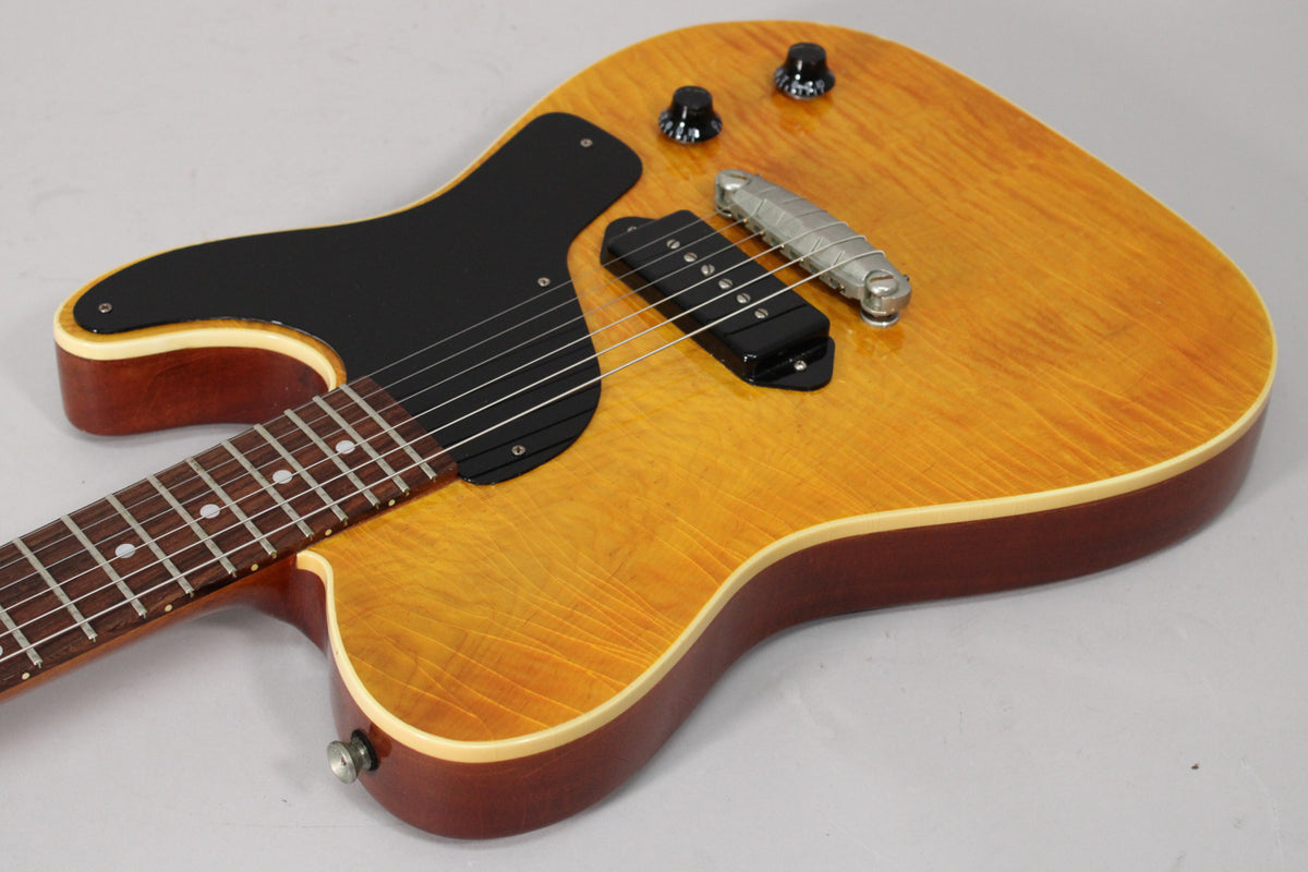 The aged amber nitro guitar body, with a black pickguard and single P90 pickup, is shown from the upper bout.