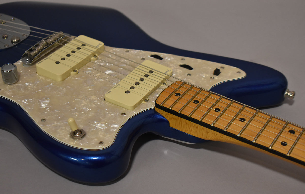 The cobalt blue Jazzmaster body, with a pearloid pickguard and cream pickups, is angled with its maple neck extending right.