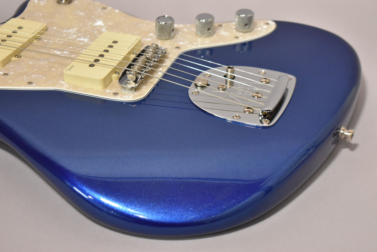 Close-up of a metallic cobalt blue Jazzmaster body, showing the pearloid pickguard, cream pickups, chrome bridge, and vibrato.