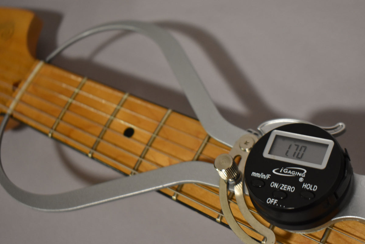 A digital caliper measures the width of the guitar's light-colored maple fretboard, showing "1.70" on its display.