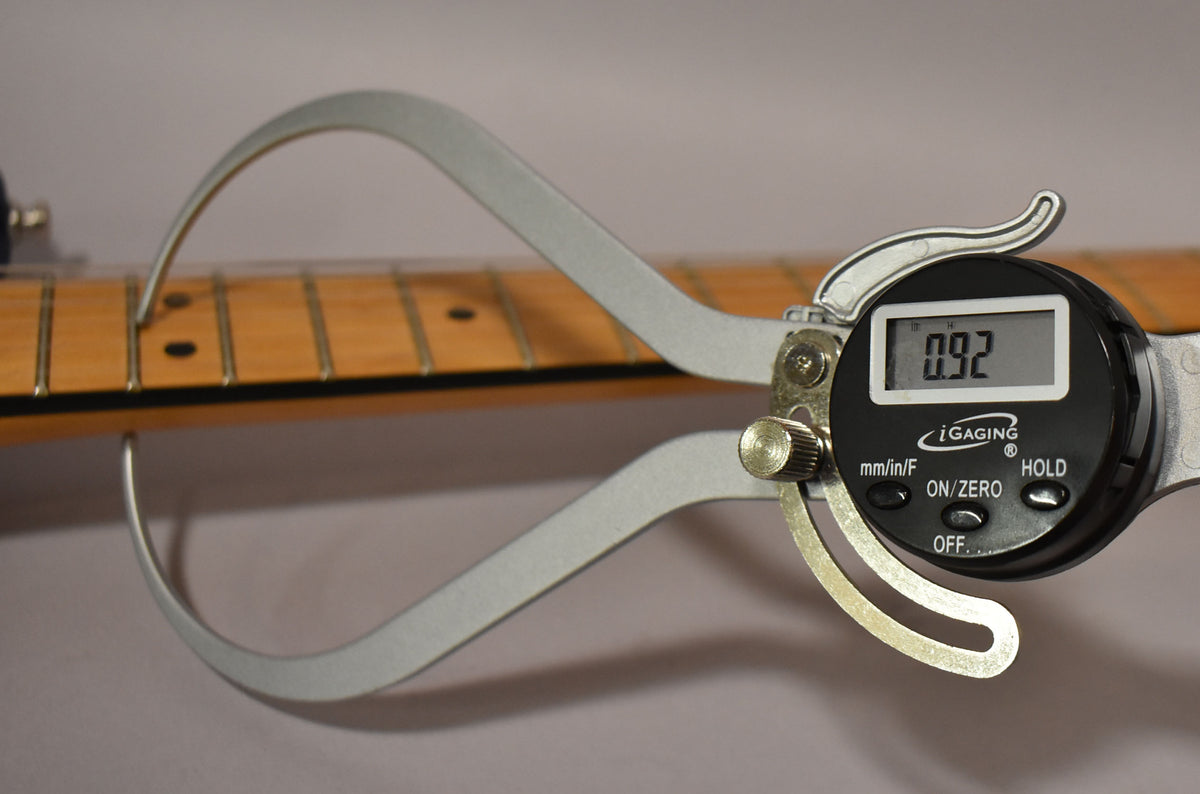 A digital caliper measures the maple fretboard's thickness at 0.92 inches, showing dark fret markers and minimal wear.