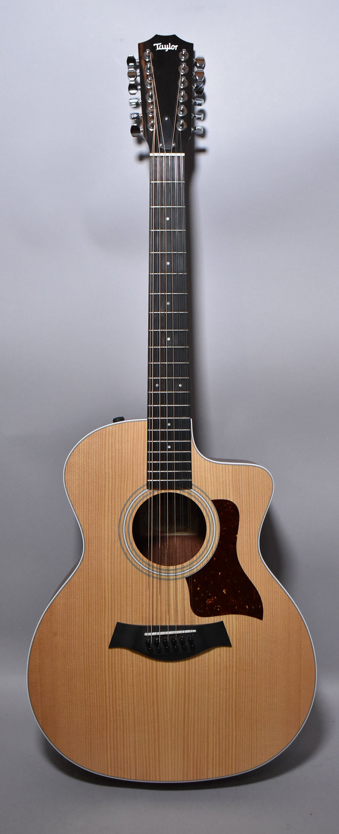 Full-length view of a natural finish 12-string acoustic guitar with a cutaway body, dark pickguard, and chrome tuners.
