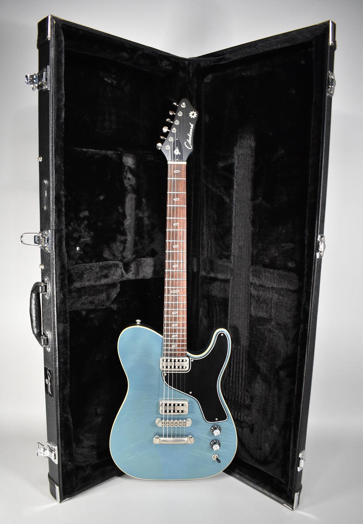 Full view of a metallic Pelham blue guitar with a black pickguard and aged hardware, standing in its open, black-lined hard case.