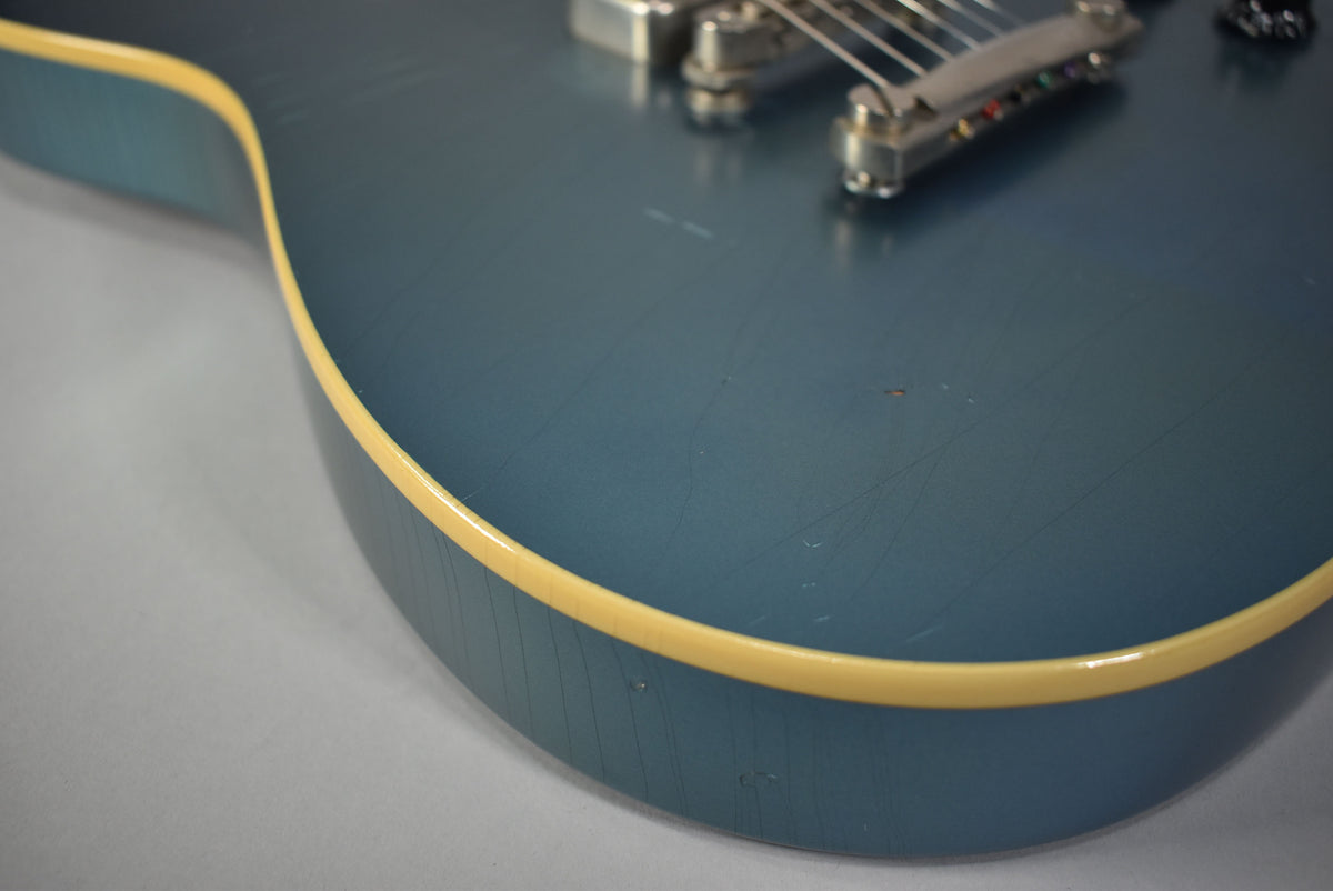 Close-up of the lower bout of a metallic Pelham Blue guitar, showing heavy finish checking, light scratches, and cream binding.