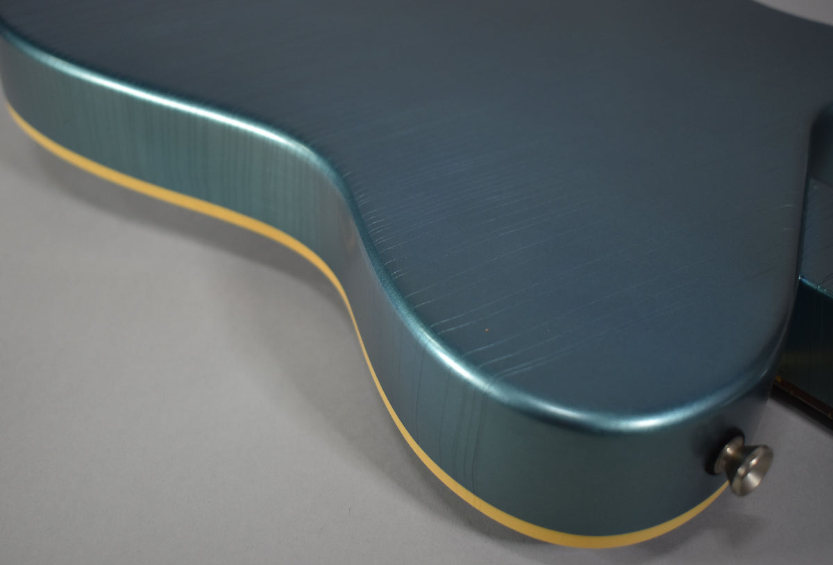 Close-up of the lower bout of a metallic Pelham blue guitar, showing heavy finish checking and cream binding, with a strap button.