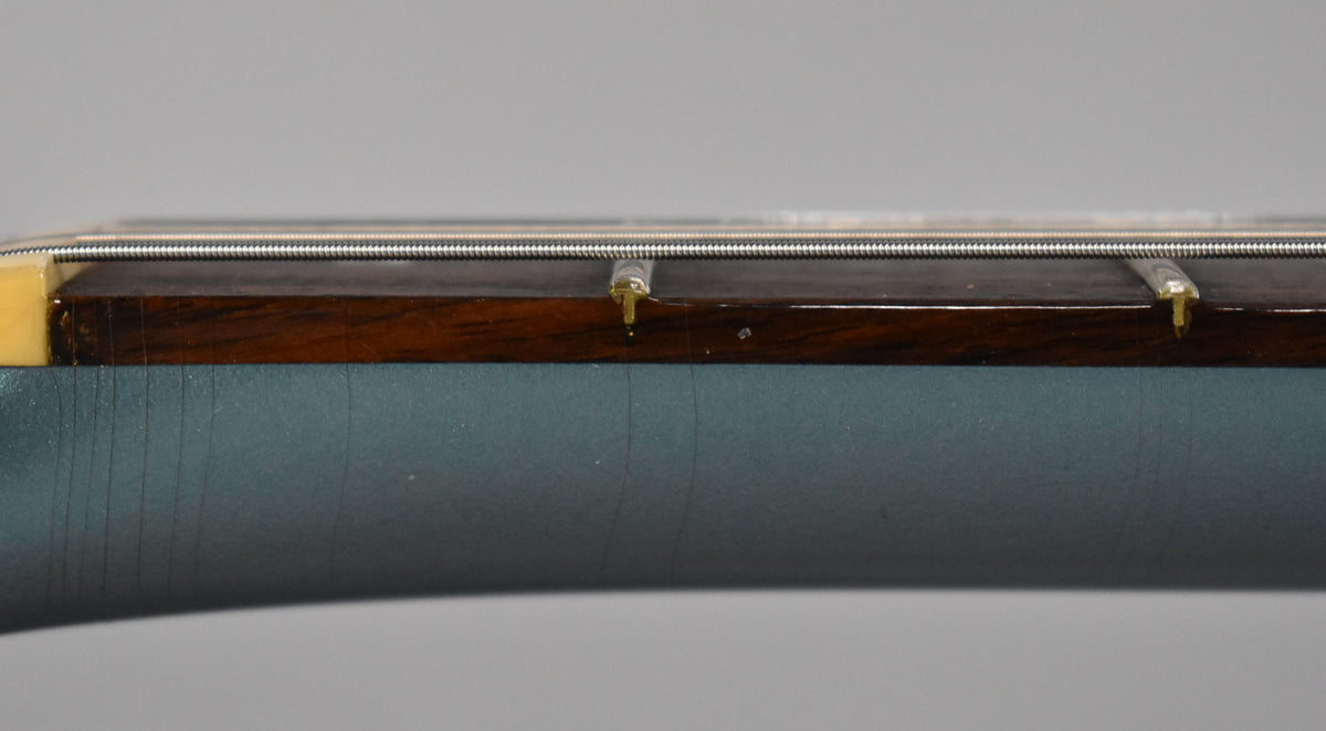 Close-up of the neck's side, showing the dark fretboard, strings, and a metallic Pelham Blue finish with vertical checking.
