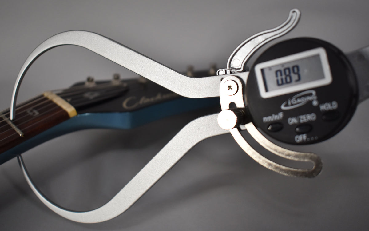 A digital caliper measures the string height at the first fret of the metallic Pelham Blue guitar, displaying "0.89".