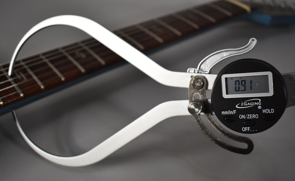A digital caliper measures the Blaster GT's fret height at 0.91, with the dark rosewood fretboard and metallic blue neck visible.
