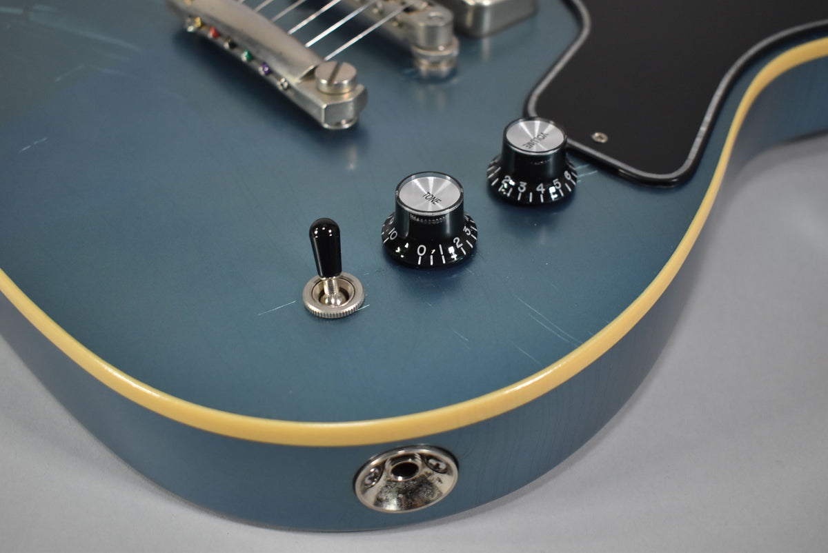 Close-up of the metallic Pelham Blue guitar body, showing two black control knobs, a toggle switch, and light surface scratches.