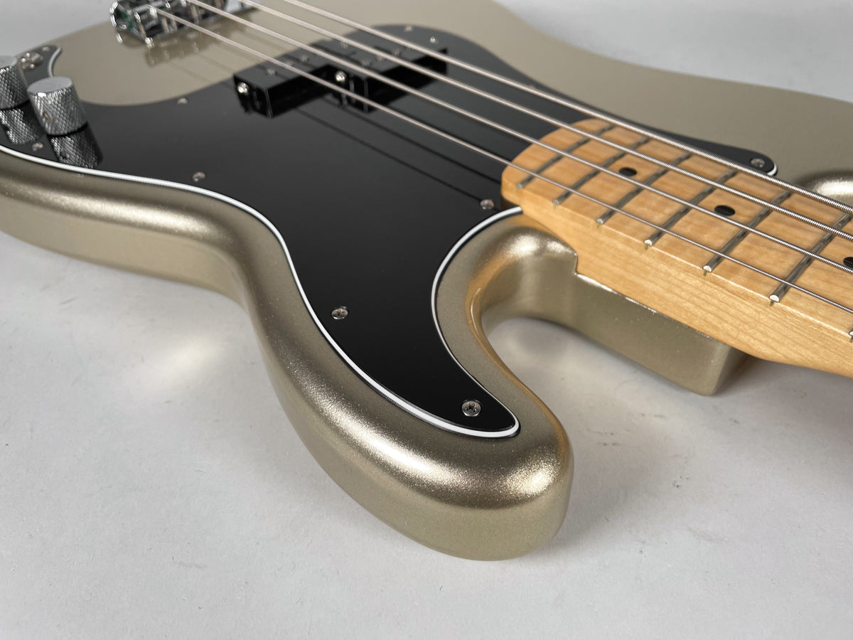 View 13: The bass body, in metallic gold with a black pickguard, is angled from the lower left, revealing two chrome knobs and a maple neck.