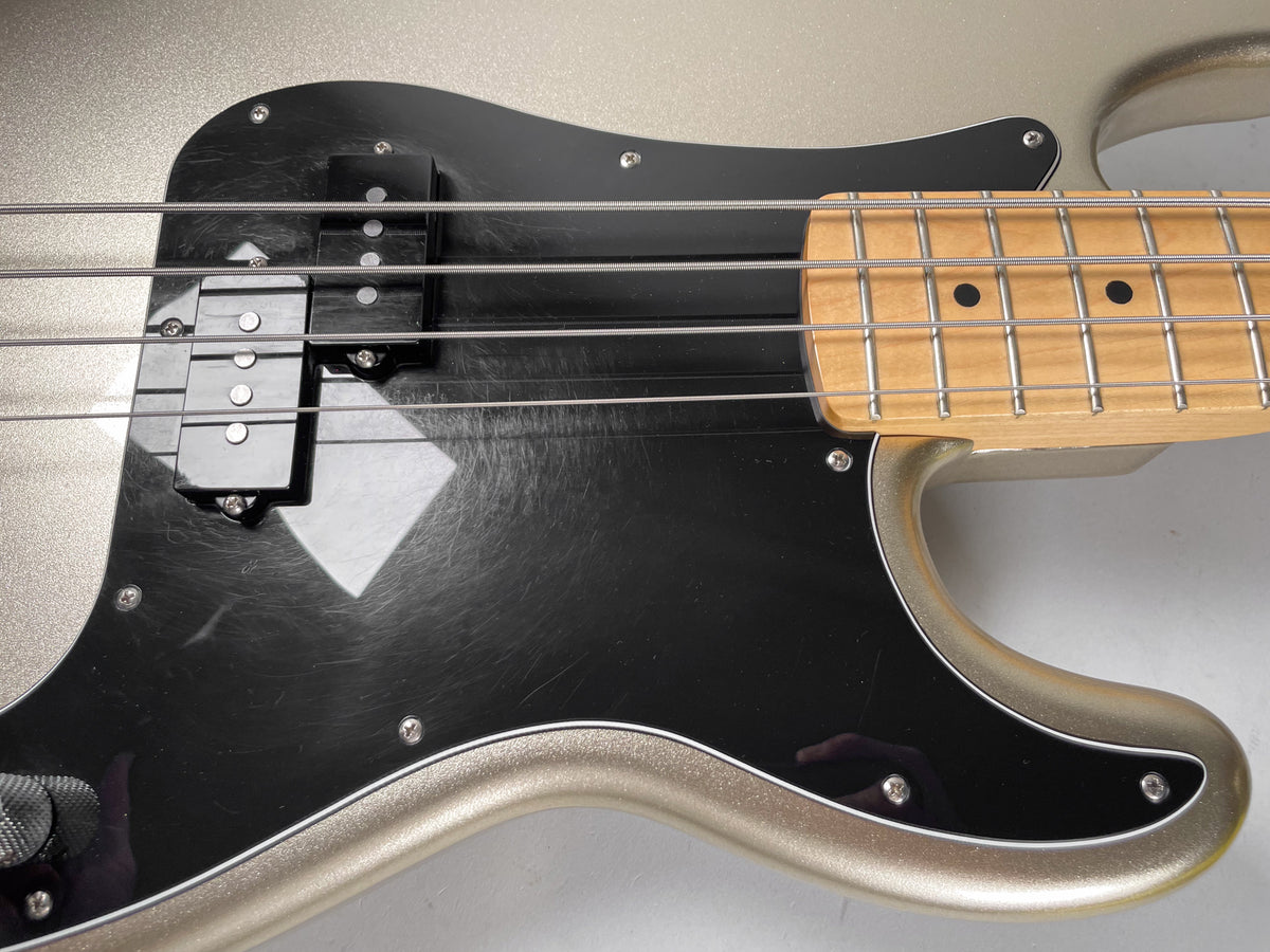 Close-up of the bass body, showing the metallic gold finish, black pickguard with visible scratches, split-coil pickup, and maple fretboard.