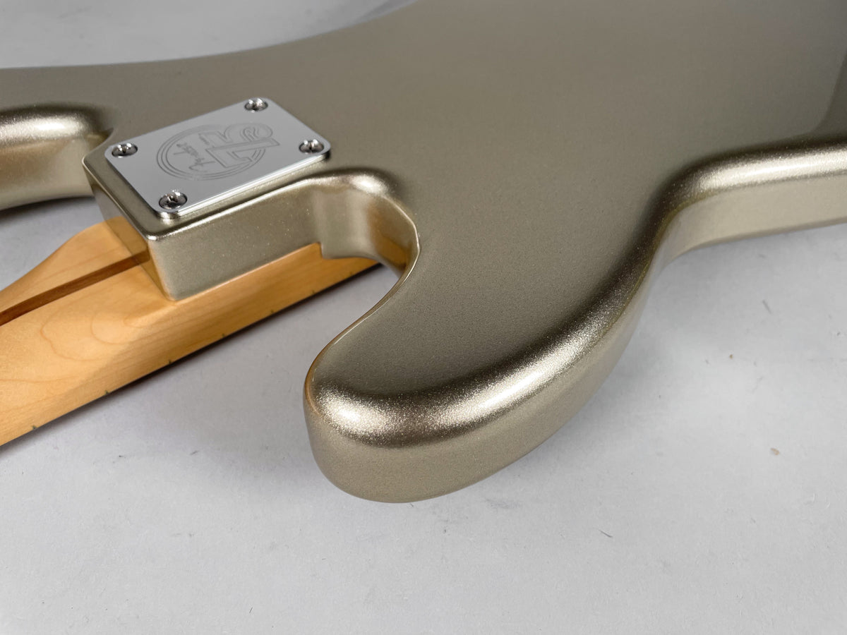 Close-up of the bass body in metallic champagne, showing the neck joint with a chrome plate and the light wood neck.