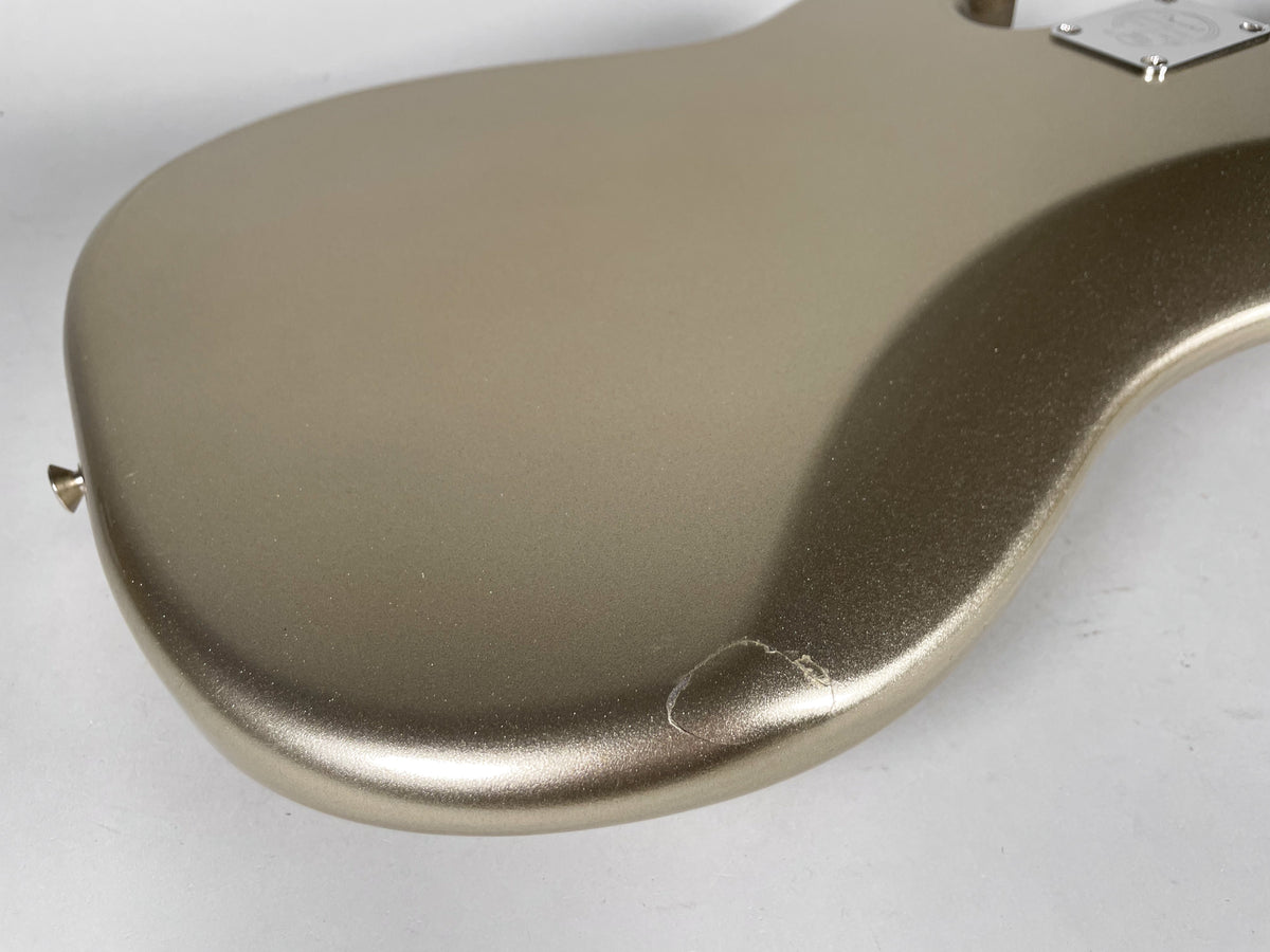 Upper body of a metallic gold bass guitar, showing a large chip in the finish on the lower bout.