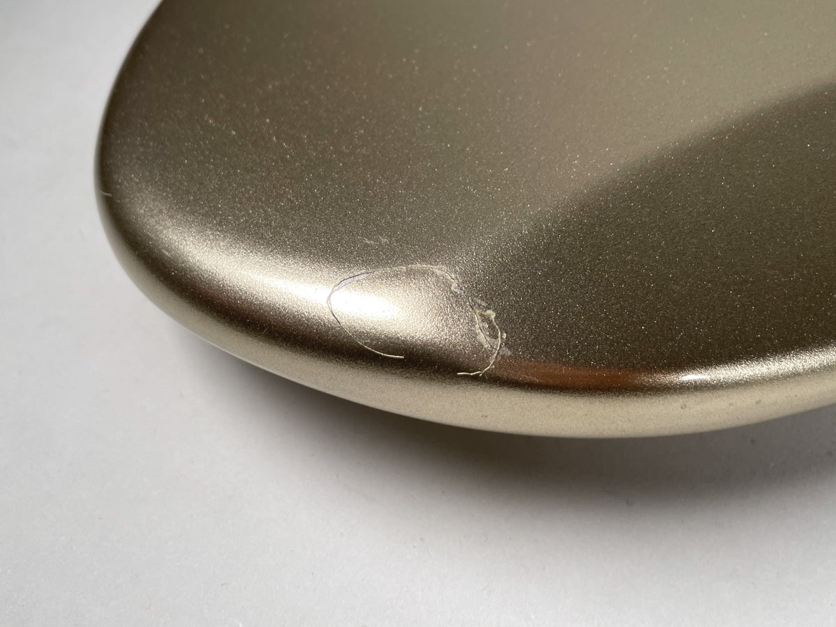 Close-up of the bass body's lower bout, showing a small chip and several scratches on the metallic gold finish.