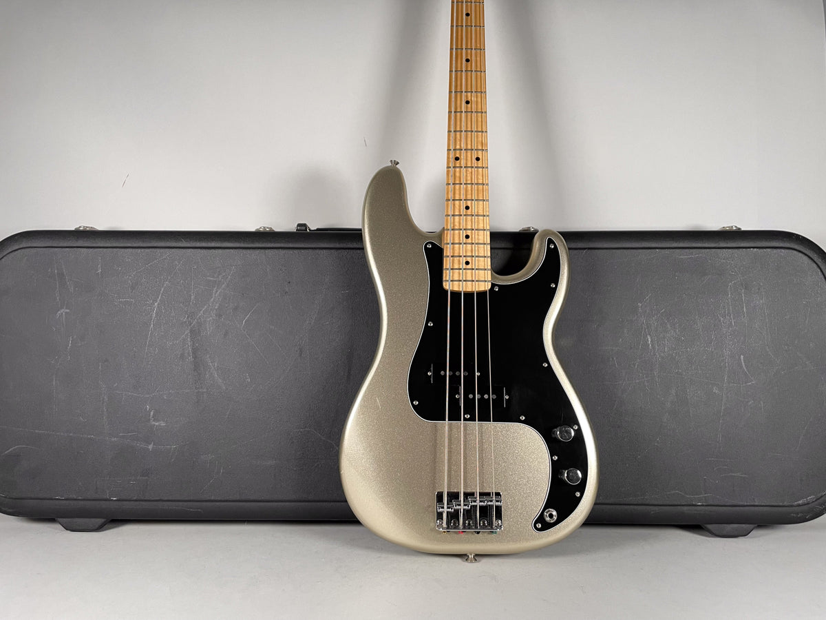 Full front view of a metallic silver bass with a black pickguard, maple fretboard, and a black hard case behind it.