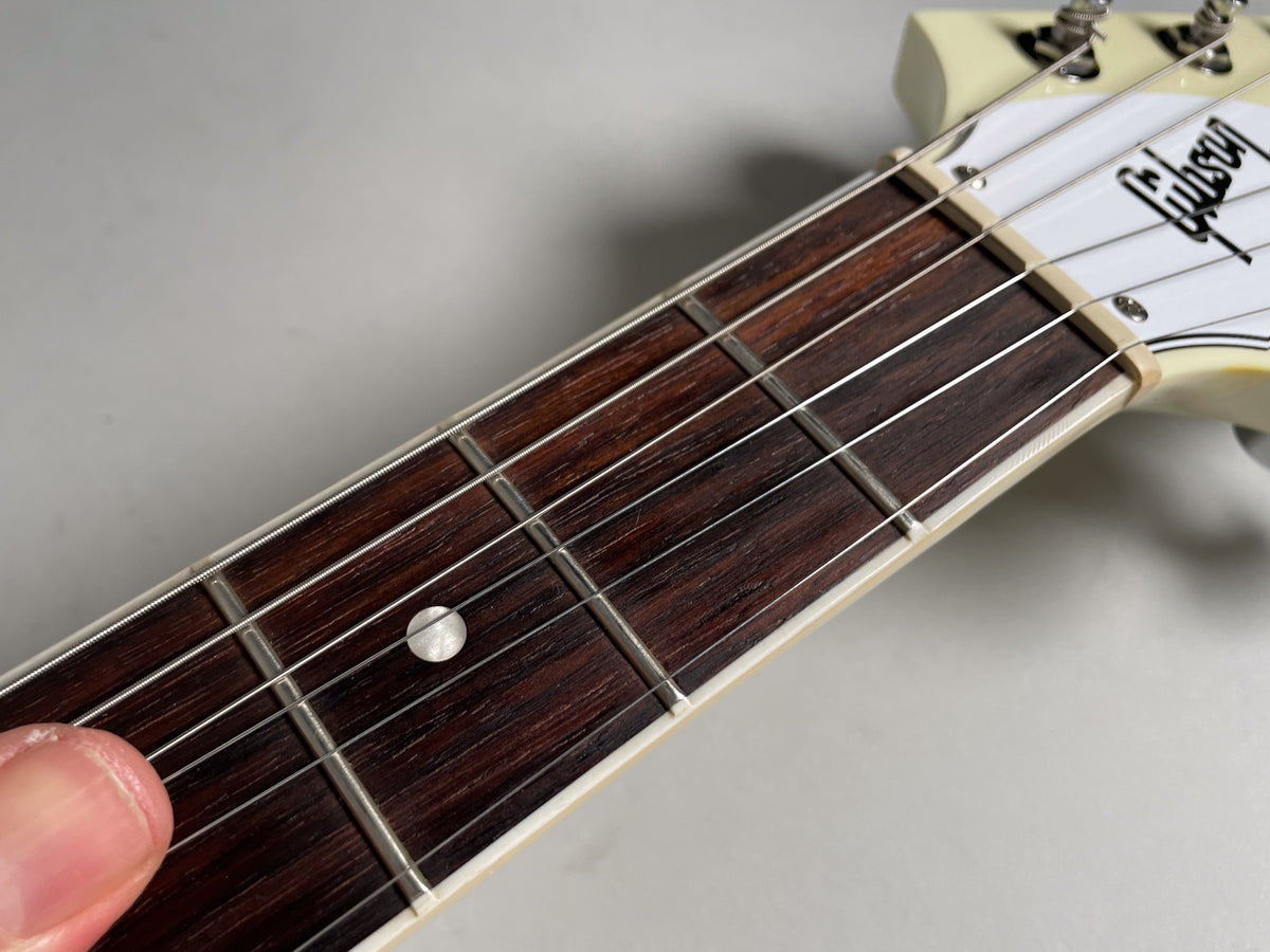 Close-up of the dark rosewood fretboard and frets, with a single pearl dot inlay at the 7th fret and a white headstock.