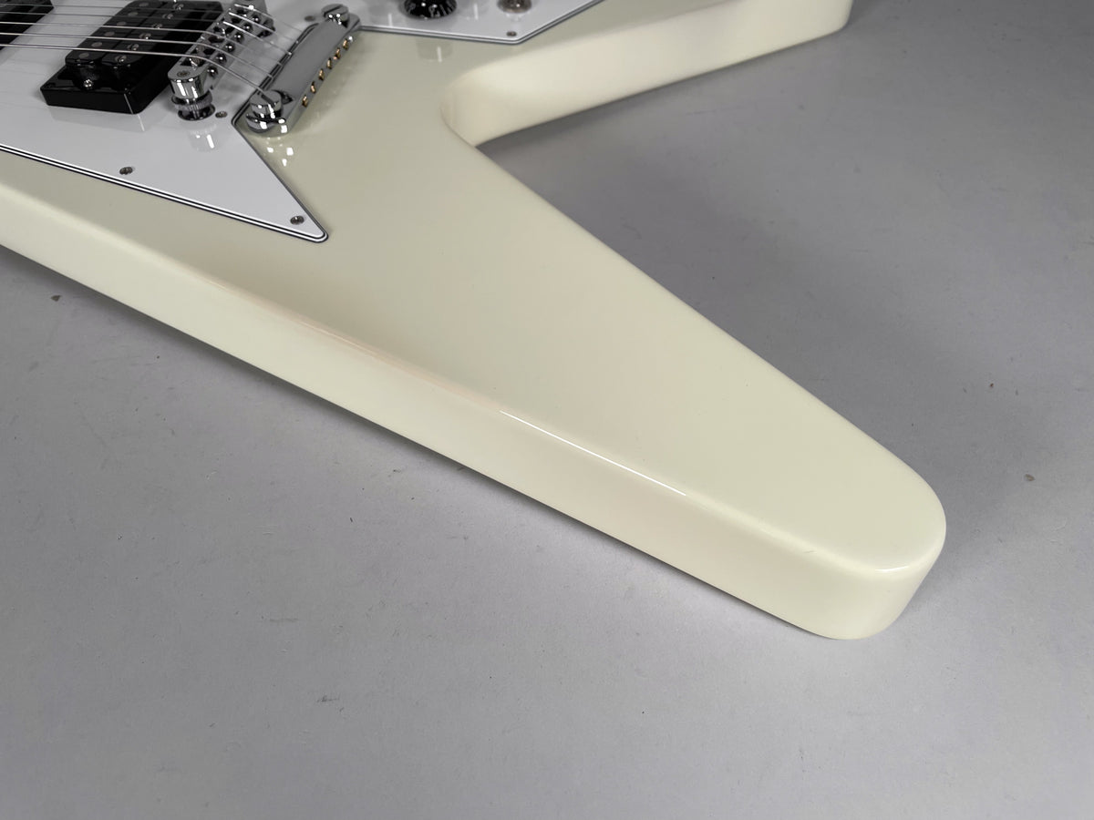 Close-up of the lower body wing of a glossy white Flying V, showing the bridge, black humbucker, and white pickguard.