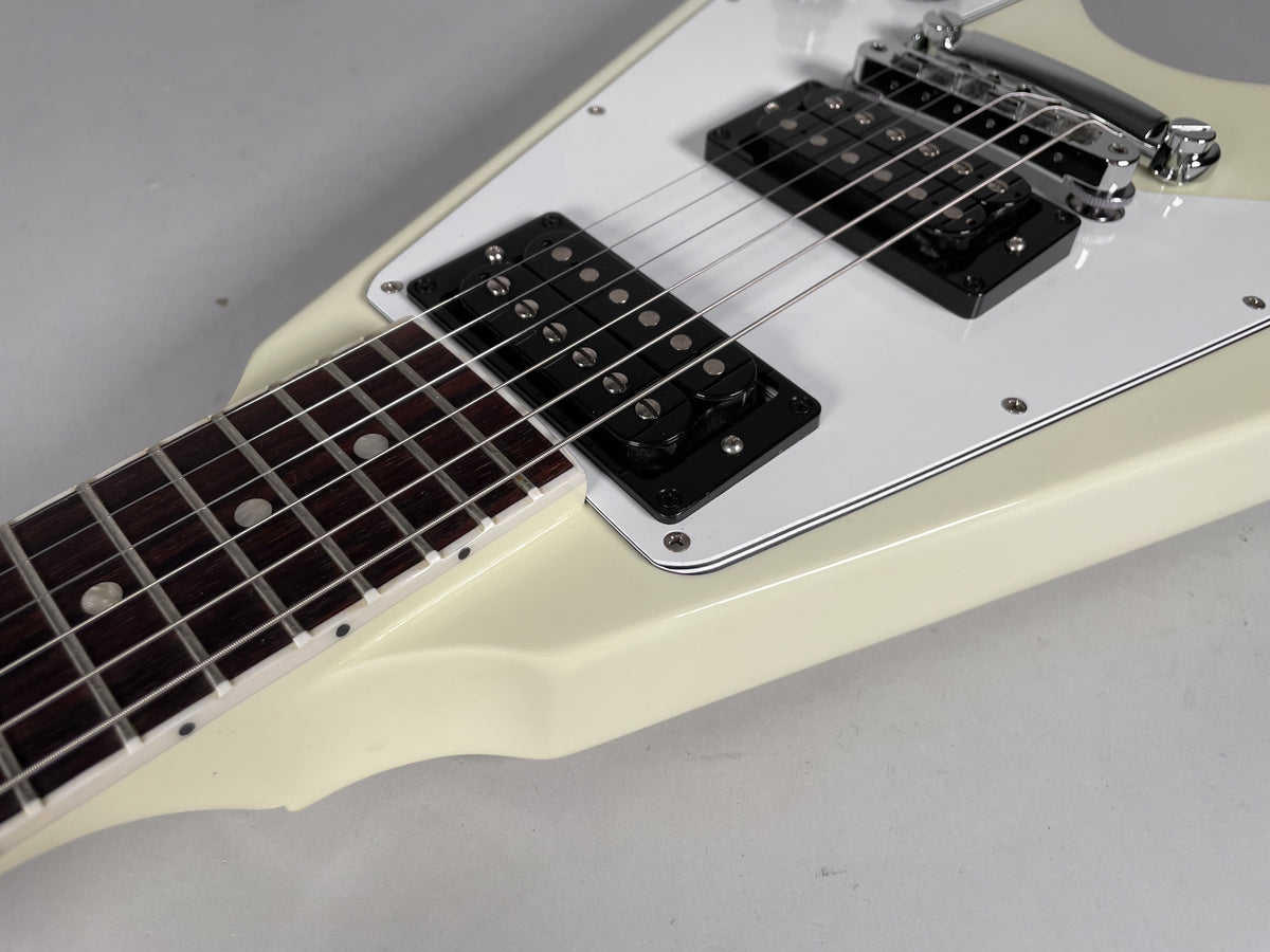Close-up of the cream Flying V's body, showing the dark fretboard, white pickguard, two black humbuckers, and chrome bridge.