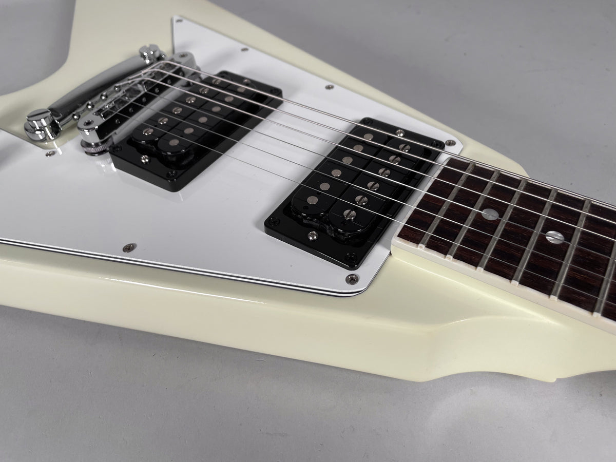 Close-up of the cream Flying V body, showing the white pickguard, two black humbuckers, and chrome tune-o-matic bridge.