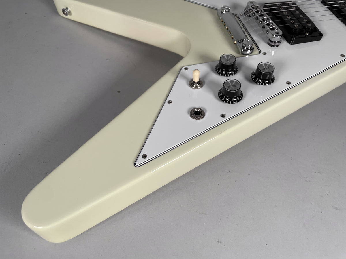 Close-up of the guitar's lower body, showing the white pickguard with three black knobs, a cream toggle switch, and input jack.