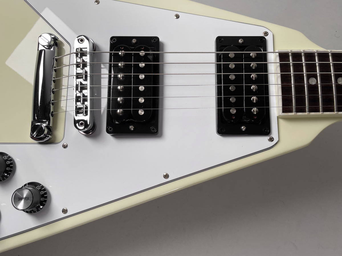 Close-up of the cream Flying V body, showing the white pickguard, two black humbuckers, chrome bridge, and two volume knobs.