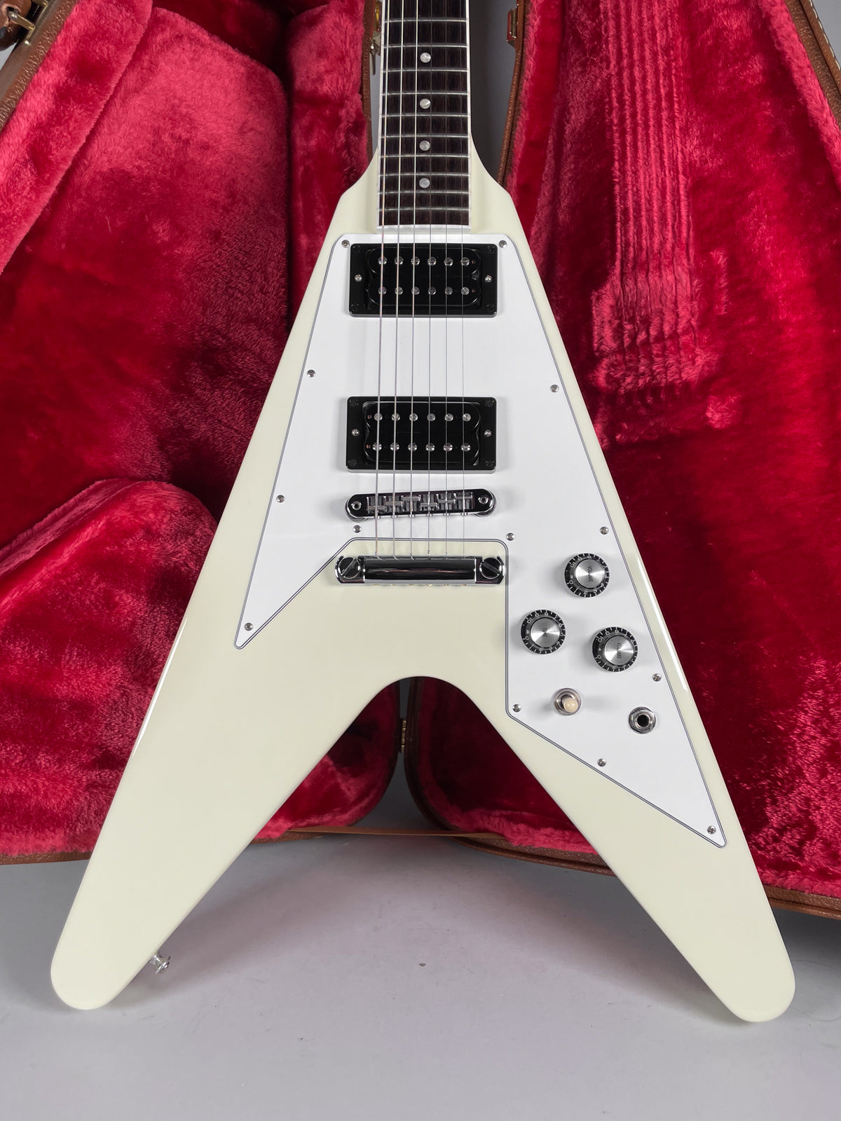 The white V-shaped electric guitar is angled, showing its body, black humbuckers, chrome hardware, and three knurled control knobs.