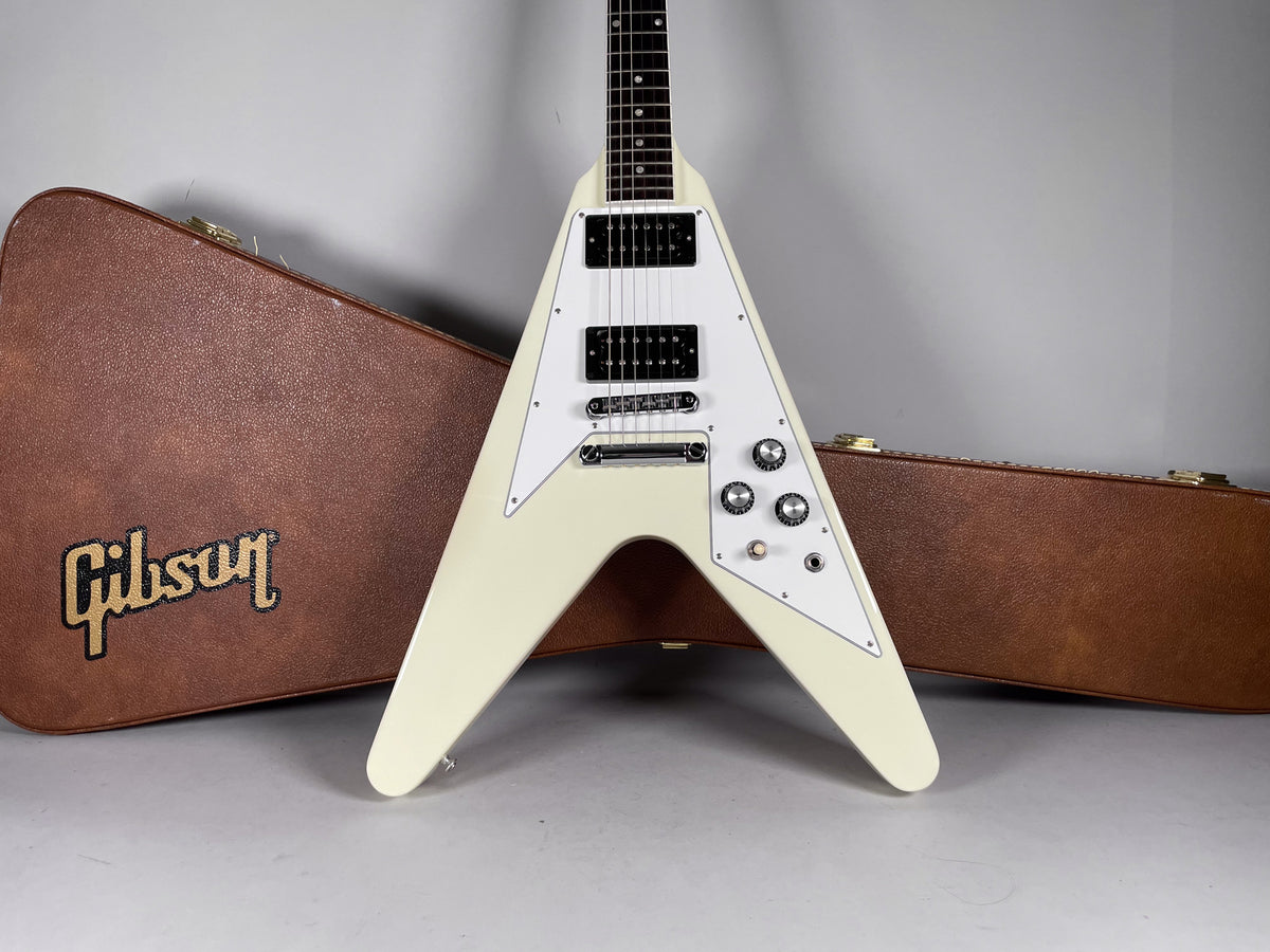 Full front view of a white Flying V electric guitar with a white pickguard, black humbuckers, and four chrome knobs.