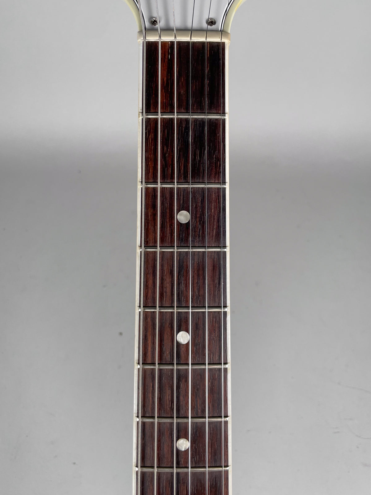 Close-up of the dark rosewood fretboard with silver frets and white dot inlays, showing the nut and first seven frets.