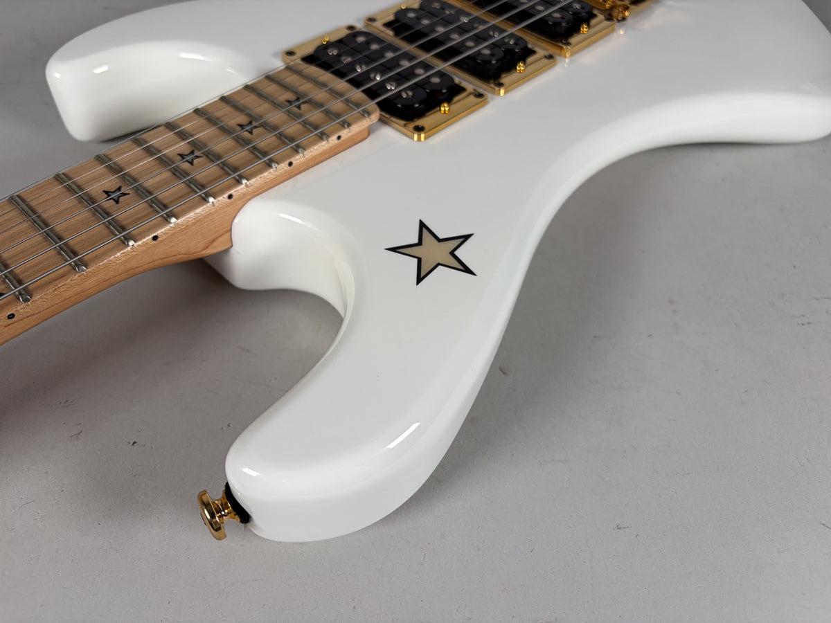 Close-up of the white guitar body with a tan star graphic, showing the lower horn, gold strap button, and part of the neck.