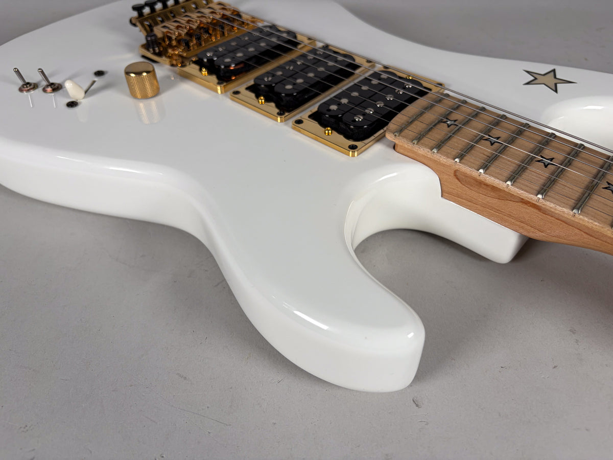 Close-up of a glossy white guitar body with gold hardware, showing the lower cutaway, pickups, and a maple fretboard with star inlays.