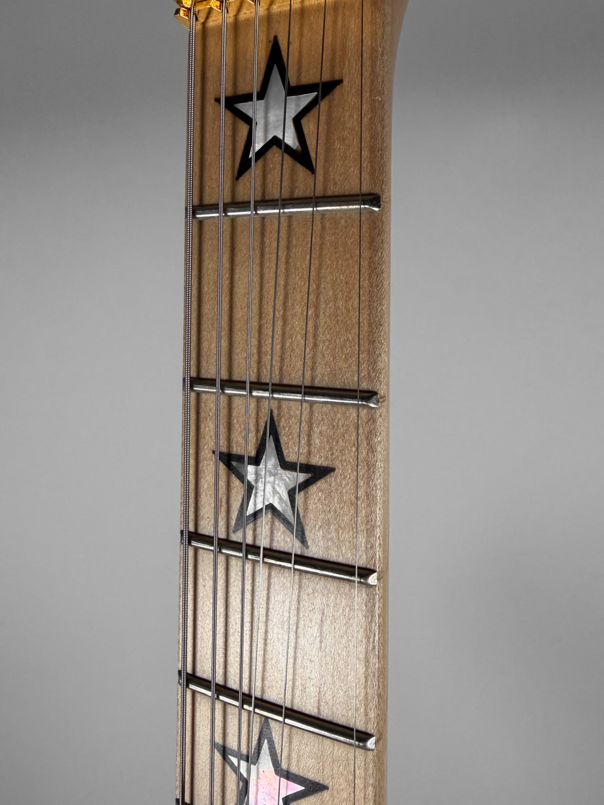 Close-up of the guitar's light wood fretboard, showing three mother-of-pearl star inlays with black outlines and six strings.