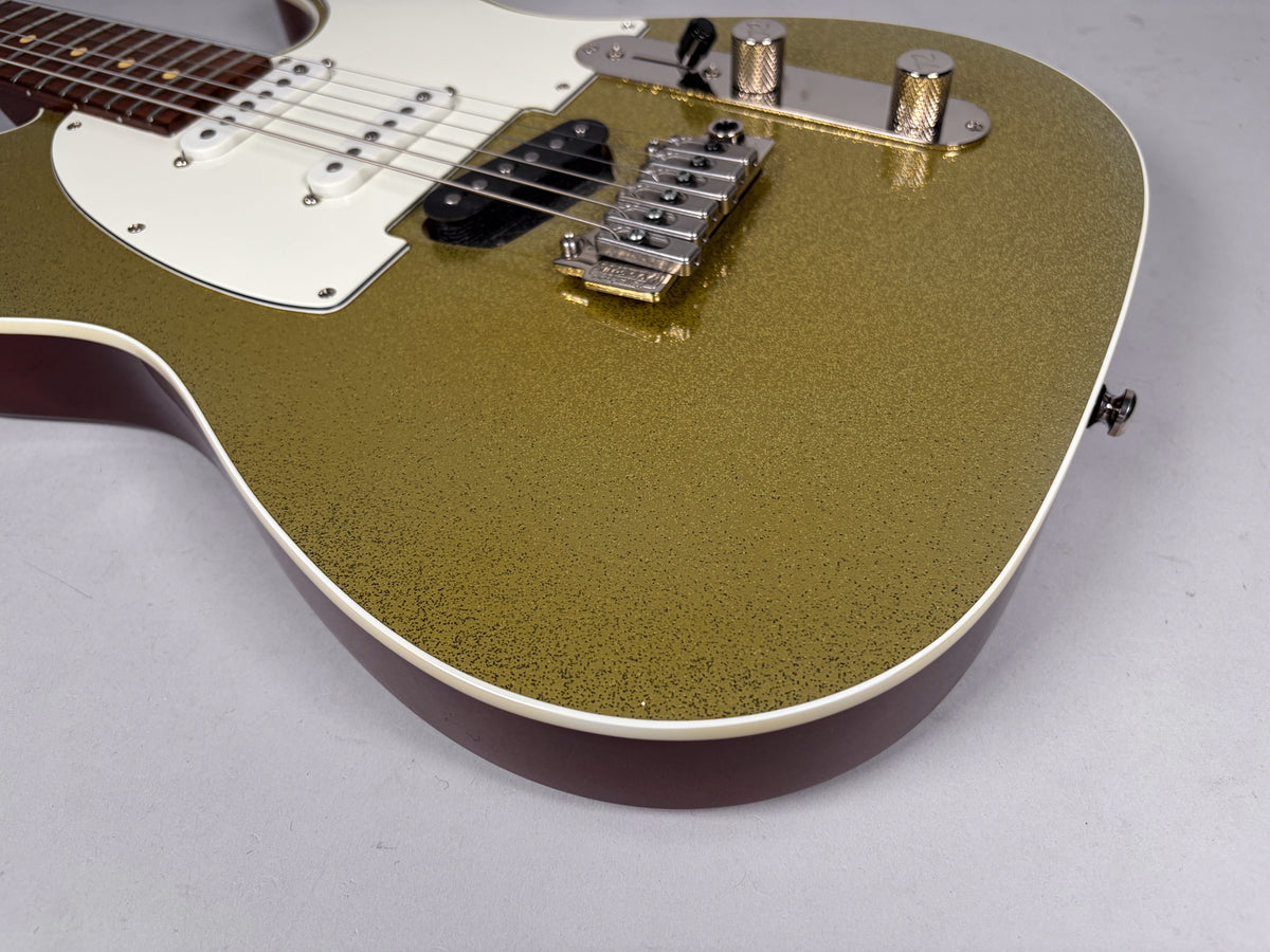 The lower bout of a gold sparkle guitar, showing the white pickguard, chrome bridge, and control plate with knurled knobs.