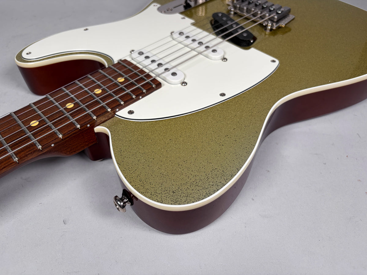 The guitar's lower body and neck are angled from the left, showing a gold sparkle finish, white pickguard, and dark wood fretboard.