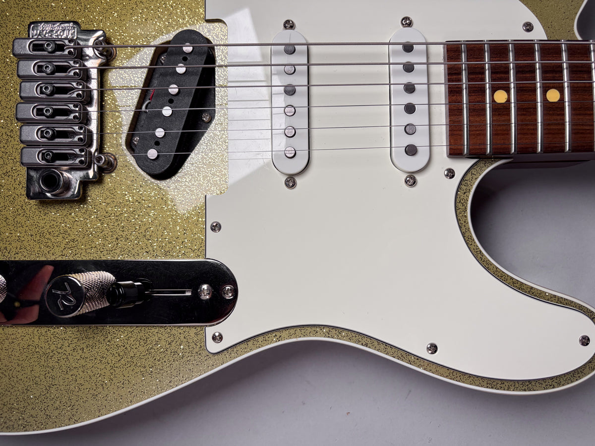 Close-up of the gold sparkle body, white pickguard, chrome bridge, black bridge pickup, and two white single-coil pickups.