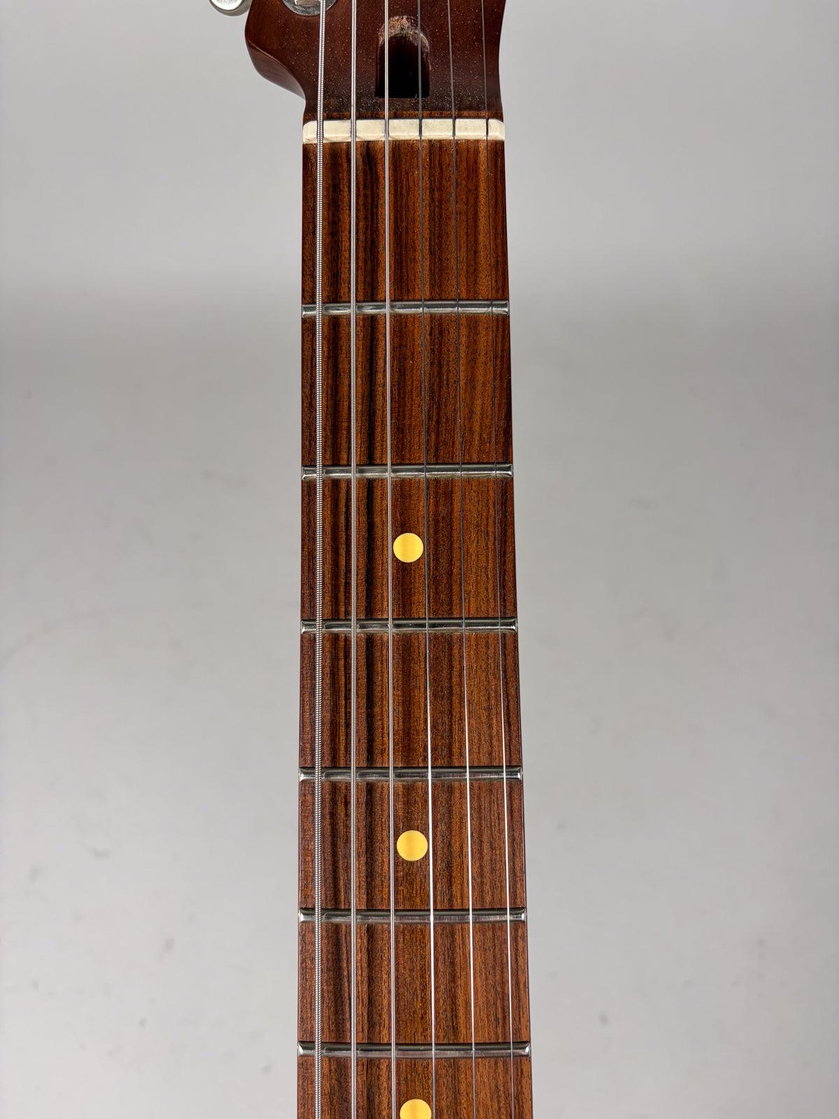 Close-up of the guitar's dark brown fretboard with yellow dot inlays, showing the nut and first few frets.