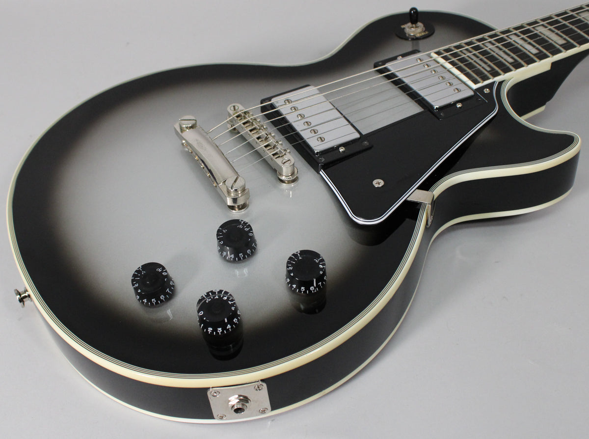 Upper body of a silverburst Les Paul, showing two humbuckers, a black pickguard, four black control knobs, and chrome hardware.