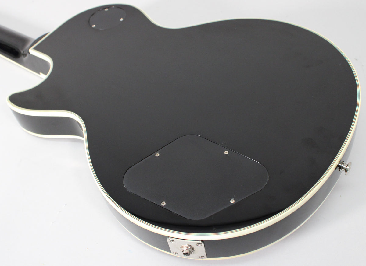 The guitar's black body, with white binding, is seen from the back, revealing two control cavity covers and a chrome output jack.